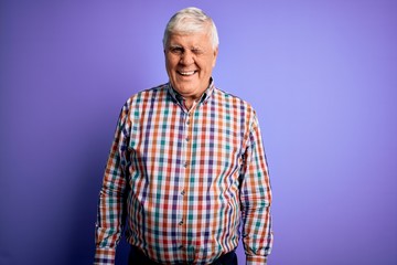 Senior handsome hoary man wearing casual colorful shirt over isolated purple background winking looking at the camera with sexy expression, cheerful and happy face.