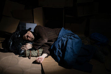 A homeless middle-aged man sleeps in cardboard boxes outside.