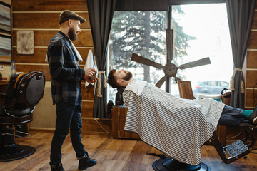 Barber in hat and bearded customer, beard cutting