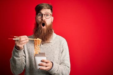 Redhead Irish man with beard holding box of ramen eating asian food using chopsticks scared in...