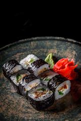 sushi roll with eel, cucumber, cream cheese, rice in plate on black wooden table background