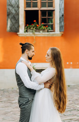 Lovely young couple hugging each other in the yard on a background of orange building.