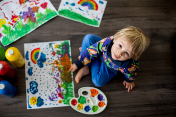 Sweet toddler blond child, boy, painting with colors, making finger prints