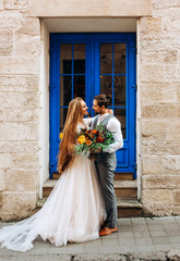 Gorgeous newlyweds with a bouquet in their hands looking at each other standing against the...
