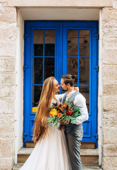 The newlyweds with a bouquet in their hands looking at each other standing against the backdrop of...