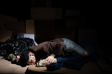A homeless middle-aged man sleeps in cardboard boxes outside.
