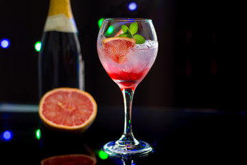 A refreshing cocktail made with grapefruit and ice on black background with lights