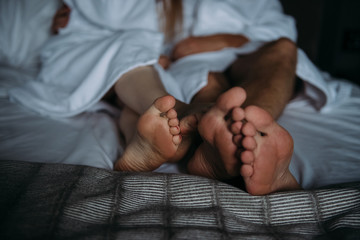 Lovers are lying on the bed in white Terry bathrobes, crossed feet close-up - 335907600