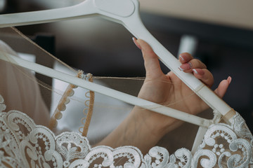 The bride is holding a hanger with a wedding dress. Close up