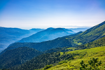 Fototapeta na wymiar View over the Green Valley, surrounded by high mountains on a summer sunset. Layers of mountains in the haze during sunset.