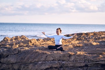 Fototapeta na wymiar Young beautiful sportwoman smiling happy practicing yoga. Coach with smile on face teaching lotus pose at the beach
