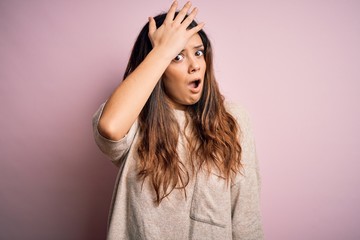 Fototapeta premium Young beautiful brunette woman wearing casual sweater standing over pink background surprised with hand on head for mistake, remember error. Forgot, bad memory concept.