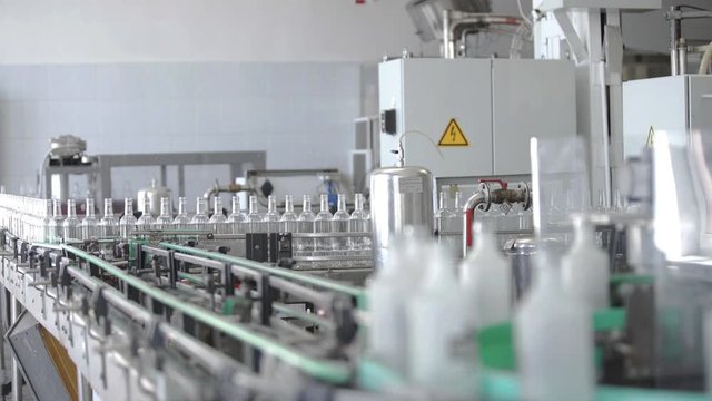 Factory for bottling alcoholic beverages. Working machine with several conveyor lines at time for production of vodka. Glass bottles in conveyor belt in distillery production line.
