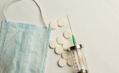 A syringe, a medical mask, and pills are on the table. Coronavirus