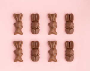 Easter bunny shaped sweets of milk chocolate laying in rows on pink background.Religious holiday composition,rabbit pattern for congratulations in greeting card.Symbol of celebration Sunday of Christ