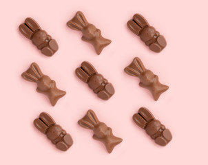 Easter bunny shaped sweets of milk chocolate laying in rows on pink background.Religious holiday composition,rabbit pattern for congratulations in greeting card.Symbol of celebration Sunday of Christ