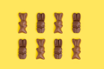 Easter bunny shaped sweets of milk chocolate laying in rows on yellow background.Religious holiday composition,rabbit pattern for congratulations, greeting card.Symbol of celebration Sunday of Christ