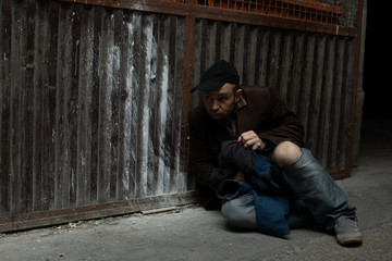 A middle-aged homeless man sits cold under a dustbin.