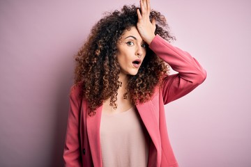 Young beautiful businesswoman with curly hair and piercing wearing elegant jacket surprised with...