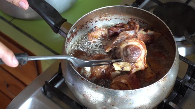 stirring with a carving fork several pieces of meat and pork fried in a pot