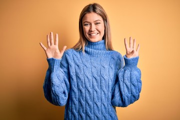 Young beautiful blonde woman wearing turtleneck sweater over yellow isolated background showing and...