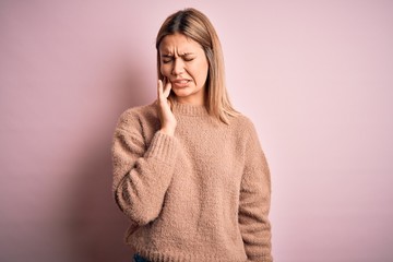 Young beautiful blonde woman wearing winter wool sweater over pink isolated background touching mouth with hand with painful expression because of toothache or dental illness on teeth. Dentist