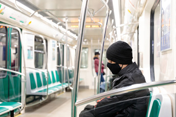 Fototapeta na wymiar Passenger in black protective mask in almost empty train of St. Petersburg subway during coronavirus pandemic. Strong decrease in passenger traffic in public transport due to quarantine measures