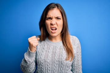 Beautiful young woman wearing casual wool sweater standing over blue isolated background angry and...