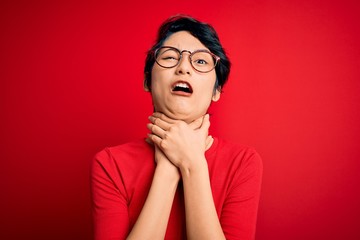 Young beautiful asian girl wearing casual t-shirt and glasses over isolated red background shouting and suffocate because painful strangle. Health problem. Asphyxiate and suicide concept.