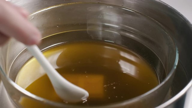 Close up of home made ointment creating process. Adding bees wax  into herbal oil base heated in water bath. 4K resolution