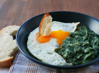 Creamed spinach with a fried egg in bowl on wooden table