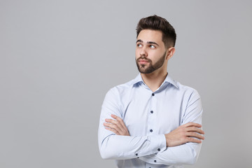 Attractive young unshaven business man in light shirt posing isolated on grey background in studio....
