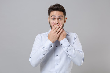Shocked young unshaven business man in light shirt posing isolated on grey wall background studio...