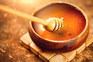Honey dripping from honey dipper in wooden bowl.  Close-up. Healthy organic Thick honey dipping...