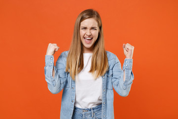 Overjoyed young woman girl in casual denim clothes posing isolated on bright orange background studio portrait. People sincere emotions lifestyle concept. Mock up copy space. Doing winner gesture.