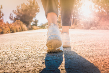 woman steps walking along a path in the forest at sunrise or sunset in nature and warm and bright light. Hiker practicing hiking.