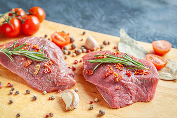 raw meat with spices, cherry tomatoes and garlic on a wooden cutting board