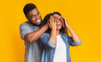 Guess who. Affectionate black man surprising his wife, covering her eyes