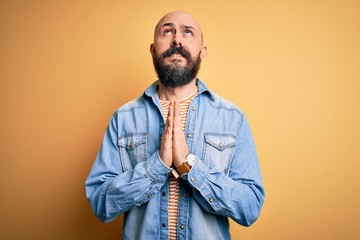 Handsome bald man with beard wearing casual denim jacket and striped t-shirt begging and praying...