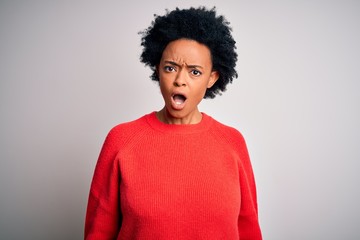 Young beautiful African American afro woman with curly hair wearing red casual sweater In shock face, looking skeptical and sarcastic, surprised with open mouth