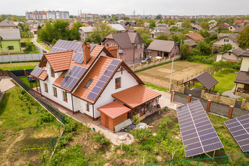 Aerial top view of new modern residential house cottage with blue shiny solar photo voltaic panels system on roof. Renewable ecological green energy production concept.