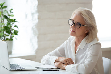Thoughtful 60 years old businesswoman using laptop business vision. Stressful mature female...