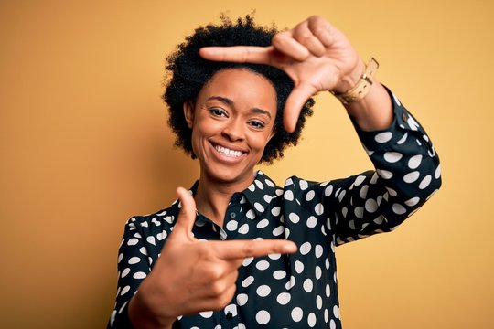 Young beautiful African American afro woman with curly hair wearing casual shirt standing smiling making frame with hands and fingers with happy face. Creativity and photography concept.