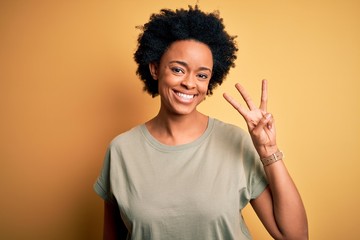 Young beautiful African American afro woman with curly hair wearing casual t-shirt showing and pointing up with fingers number three while smiling confident and happy.