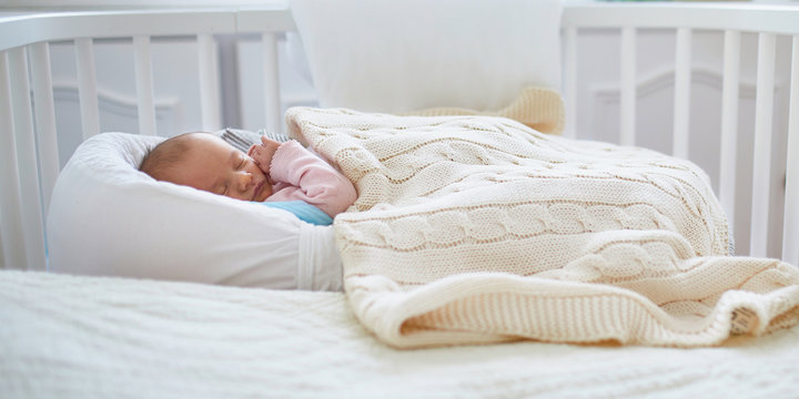 Newborn baby having a nap in co-sleeper crib attached to parents' bed