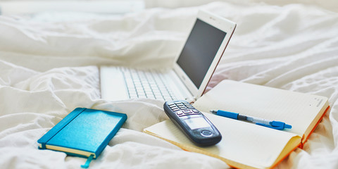 Laptop, notebook and phone in bed on clean white linens