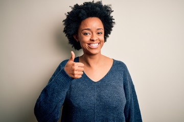 Young beautiful African American afro woman with curly hair wearing casual sweater doing happy thumbs up gesture with hand. Approving expression looking at the camera showing success.