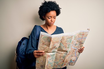 Young African American afro tourist woman with curly hair wearing backpack using city map with a confident expression on smart face thinking serious