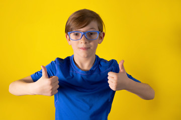 Closeup of female hand showing thumbs up sign against pastel yellow background. Funny boy 9 years old close up on an orange background