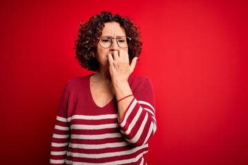Fototapeta na wymiar Middle age beautiful curly hair woman wearing casual striped sweater over red background looking stressed and nervous with hands on mouth biting nails. Anxiety problem.